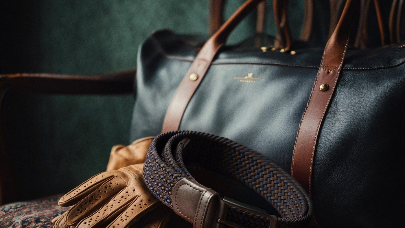 Braided stretch belt with leather tips resting on a leather weekender bag